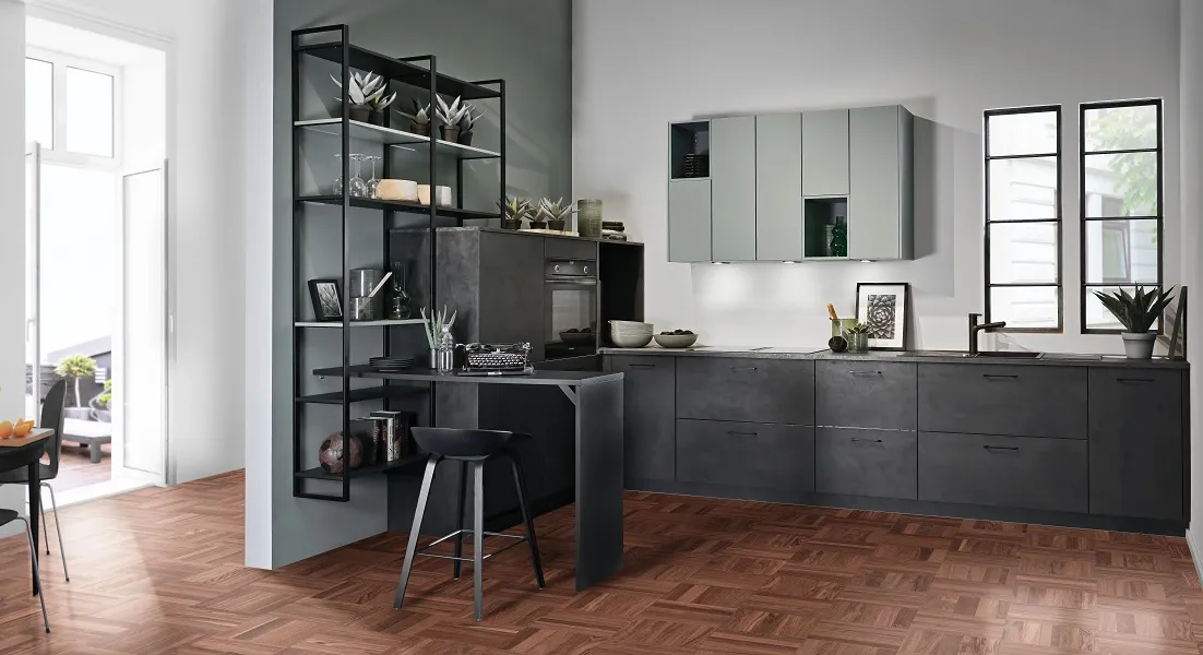 Cuisine moderne industrielle façades effet béton foncé et étagères en métal noir, dynamisée par de jolis meubles hauts et niches coloris vert sauge